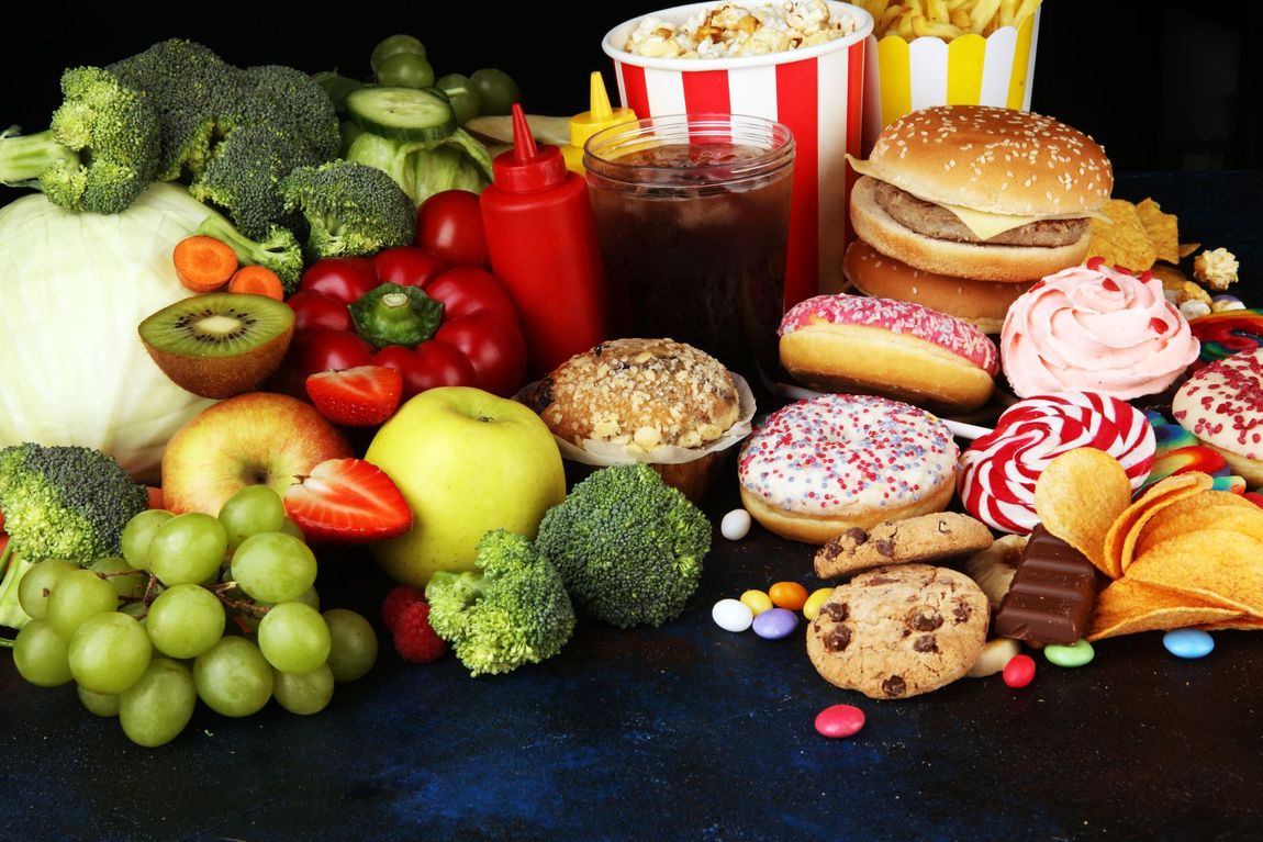 Obst, Gemüse und Junkfood. Gesunde und ungesunde Lebensmitteloptionen auf einer dunklen Oberfläche.