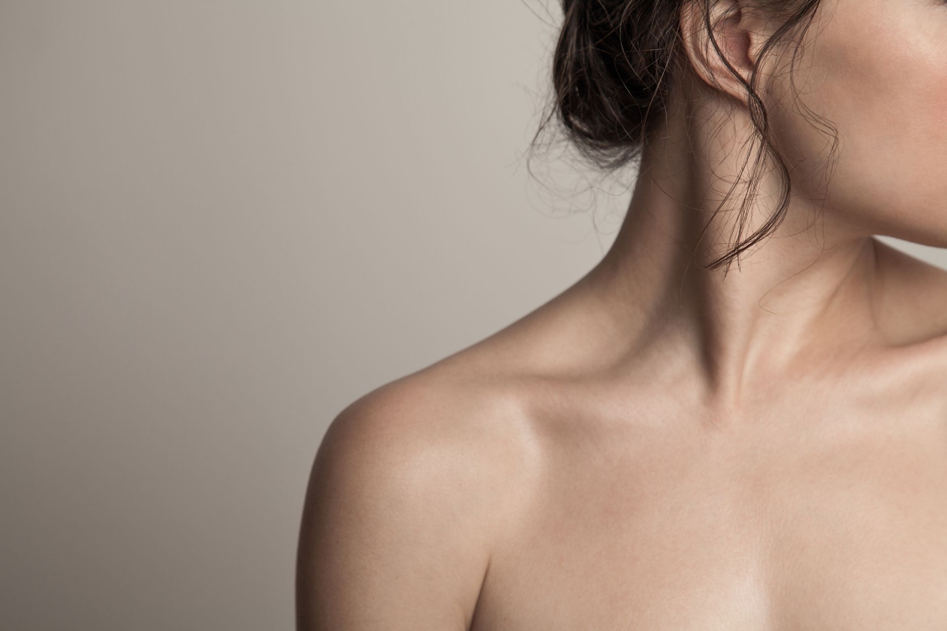 Mulher usando uma ferramenta branca de gua sha na bochecha em um banheiro, olhando no espelho.