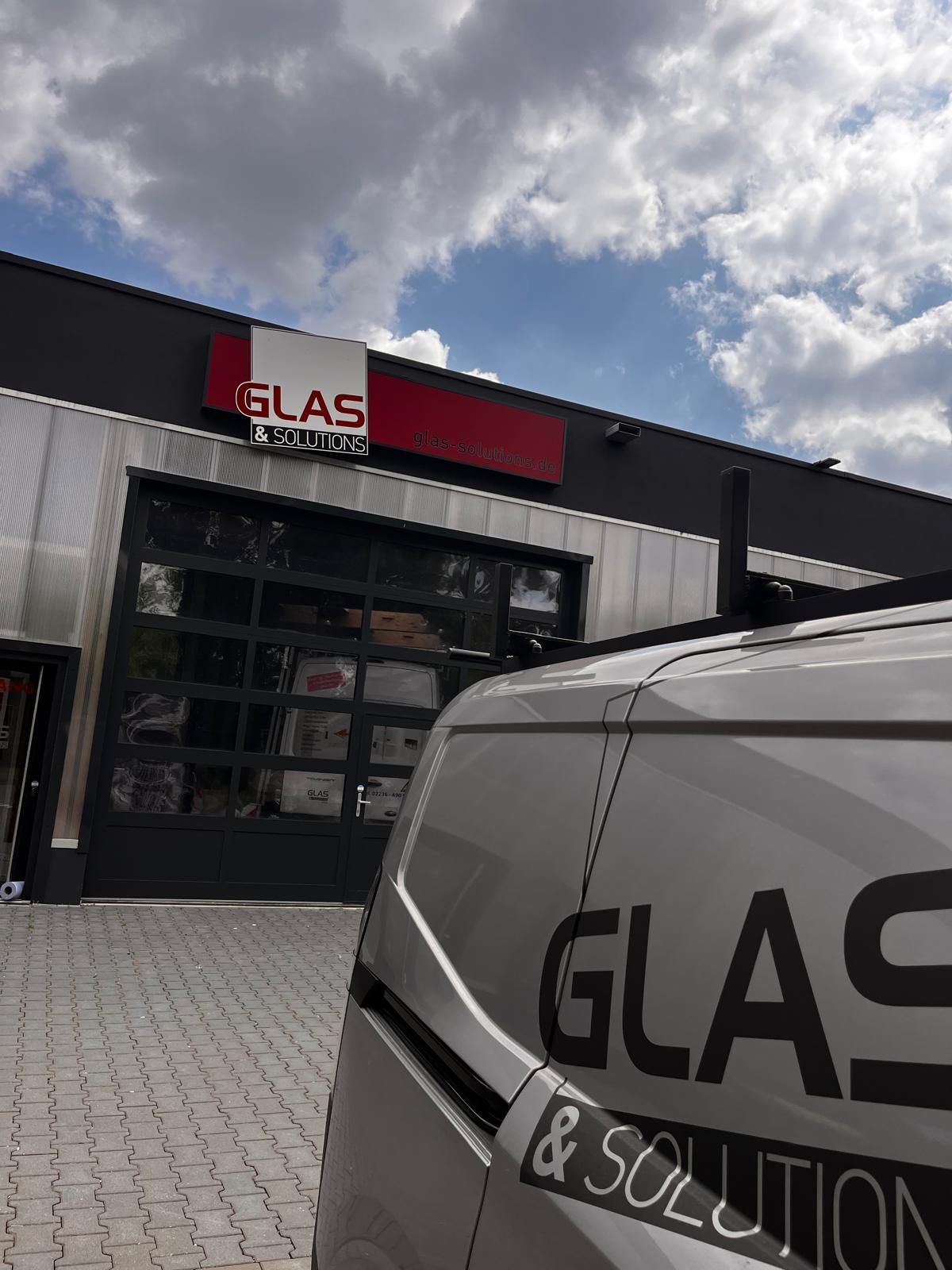 Schaufenster von Glass & Solution mit schwarz-rotem Schild, daneben ein weißer Firmenwagen.