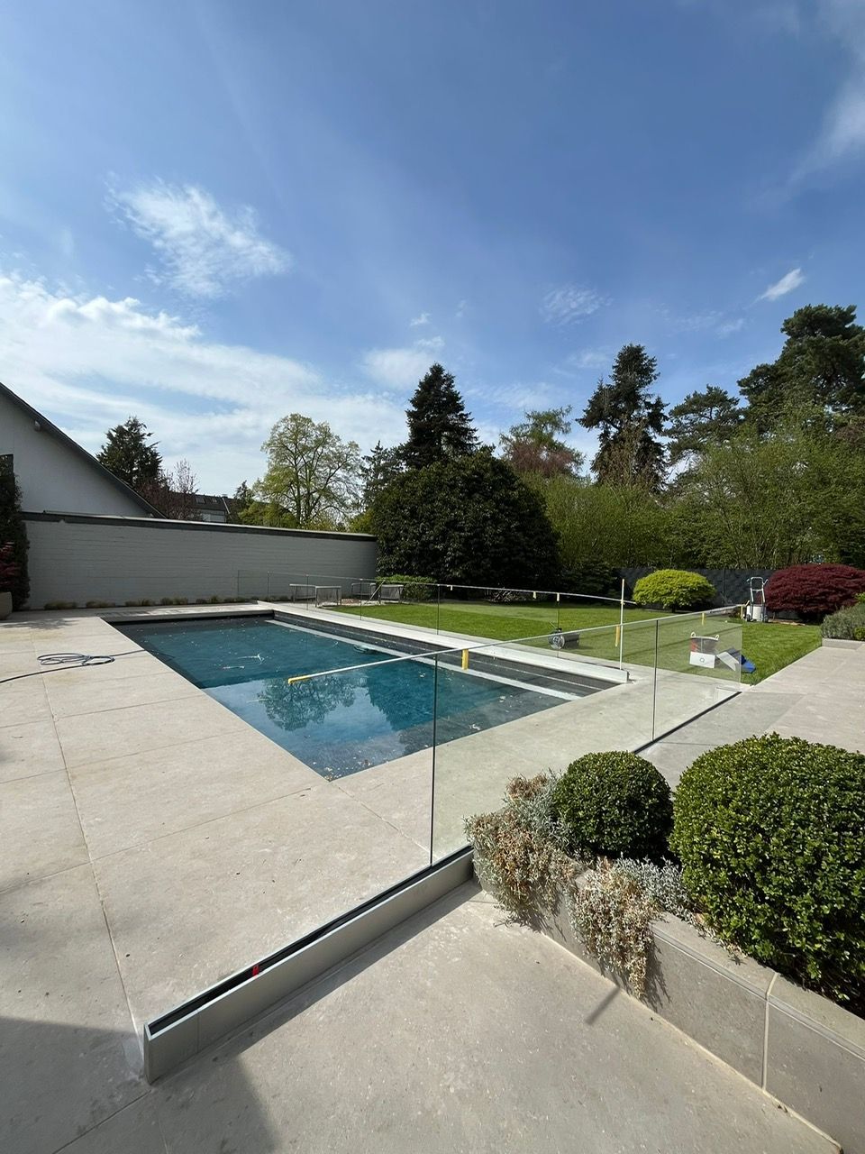 Moderner Garten mit rechteckigem Swimmingpool, weißer Terrasse, geschnittenen Hecken und blauem Himmel