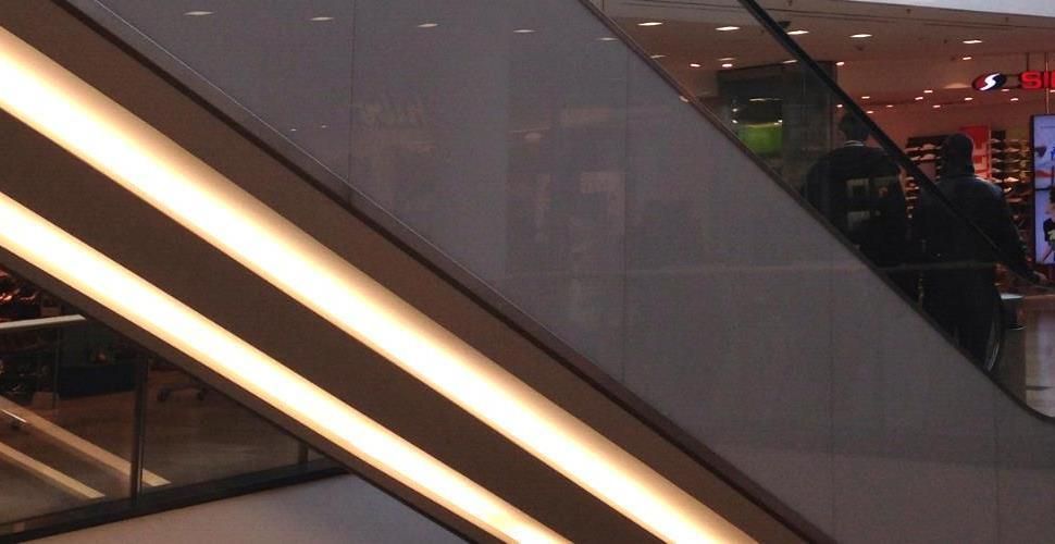 Eine Rolltreppe in einem Einkaufszentrum mit der Spiegelung eines Ladens