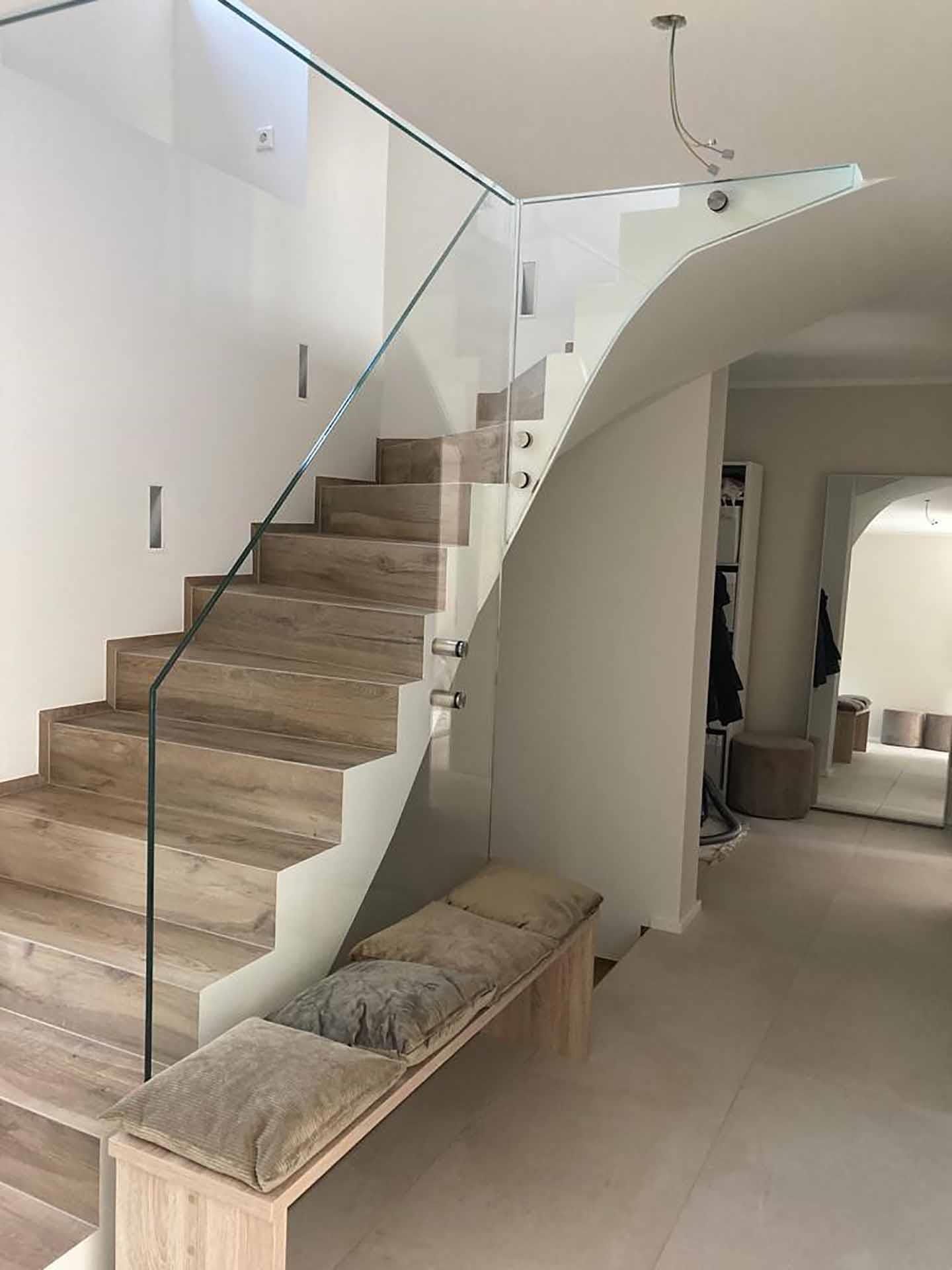 Eine Treppe mit Glasgeländer und einer Bank darunter.