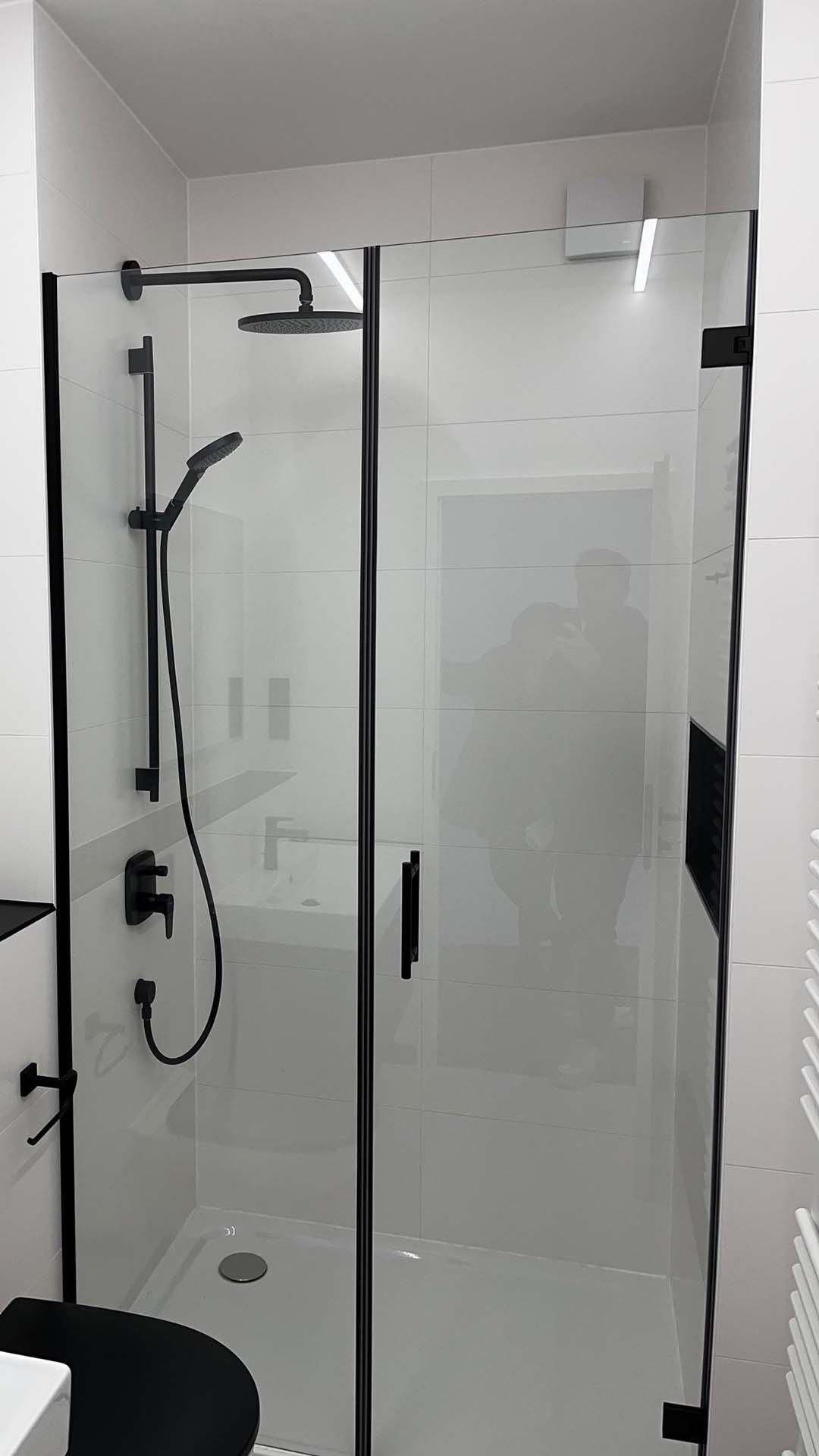 Eine Duschkabine mit schwarzem Rahmen und Duschkopf in einem Badezimmer.