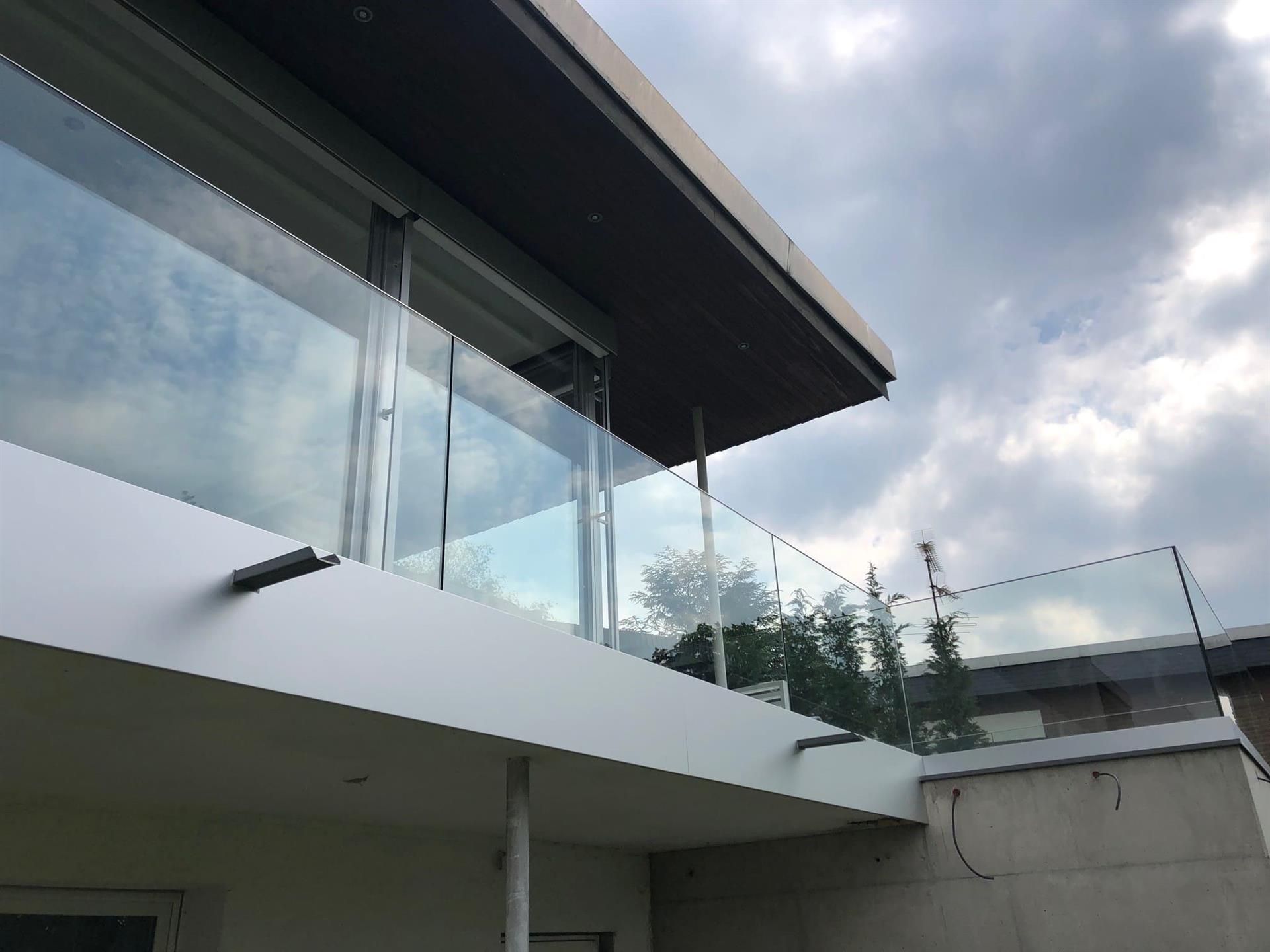 Ein Balkon mit Glasgeländer und einem bewölkten Himmel im Hintergrund