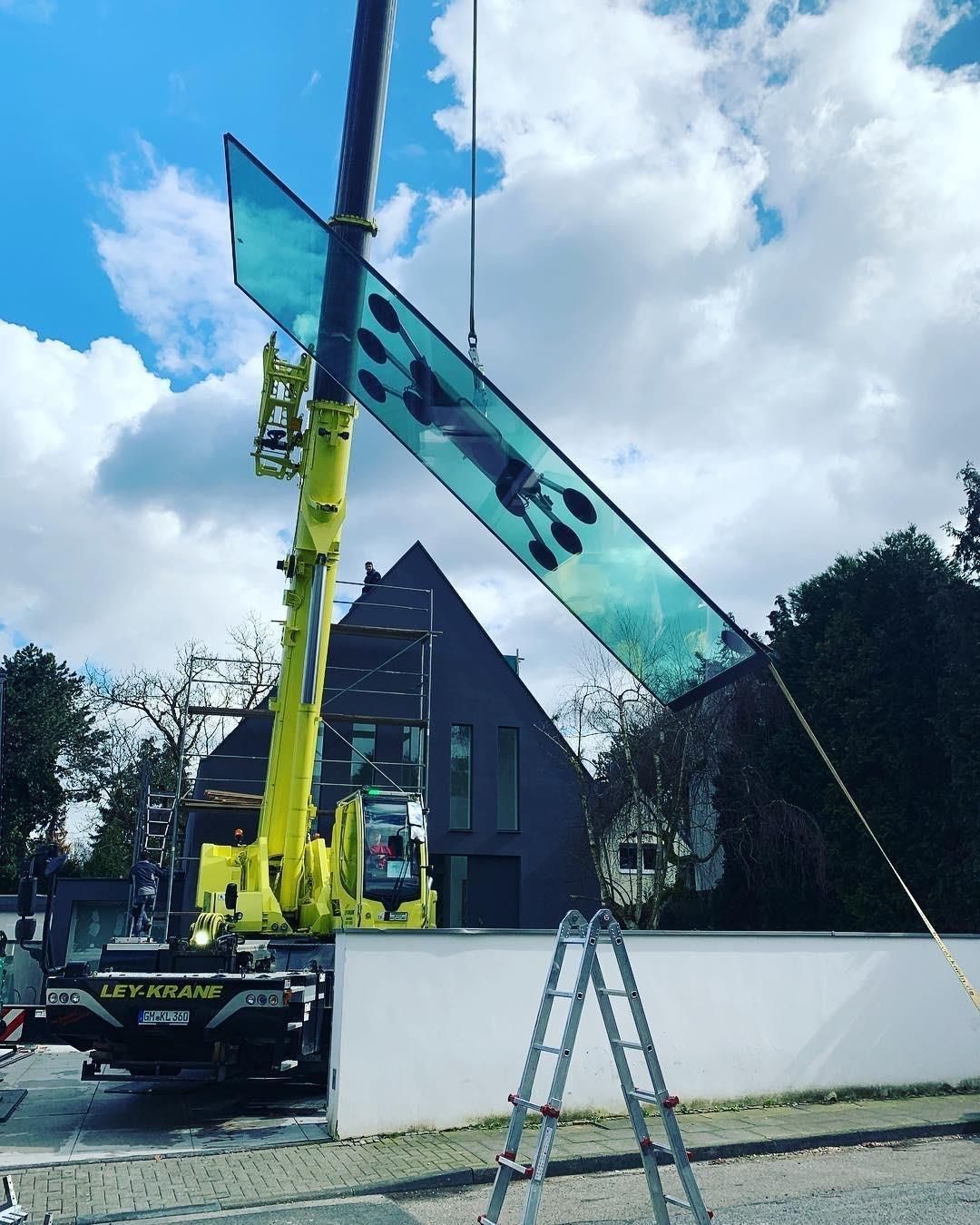 Ein gelber Kran hebt ein großes Stück Glas