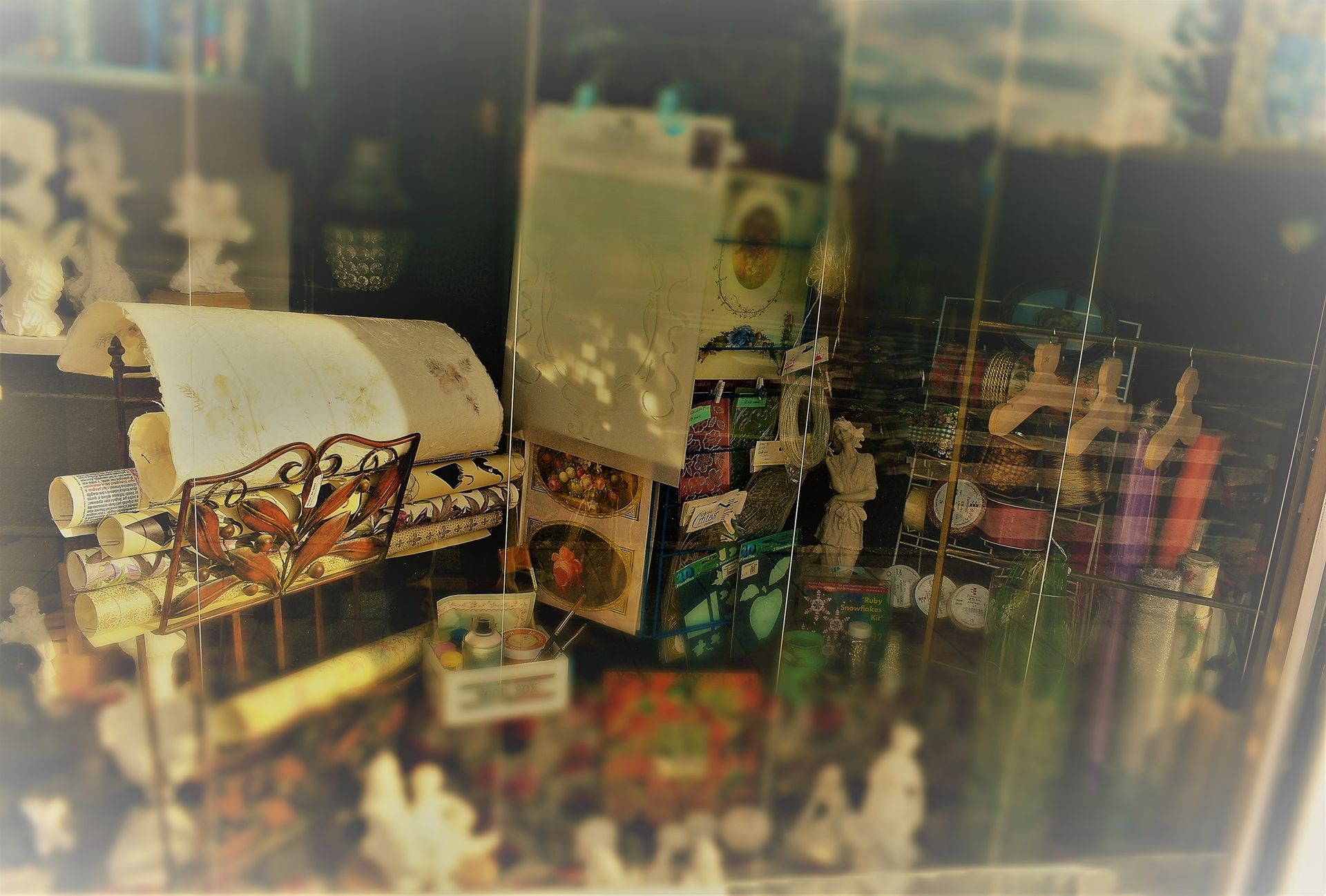 Una vitrina de tienda desordenada con artículos coloridos, incluidos modelos de barcos, figuras y una pequeña caja blanca.