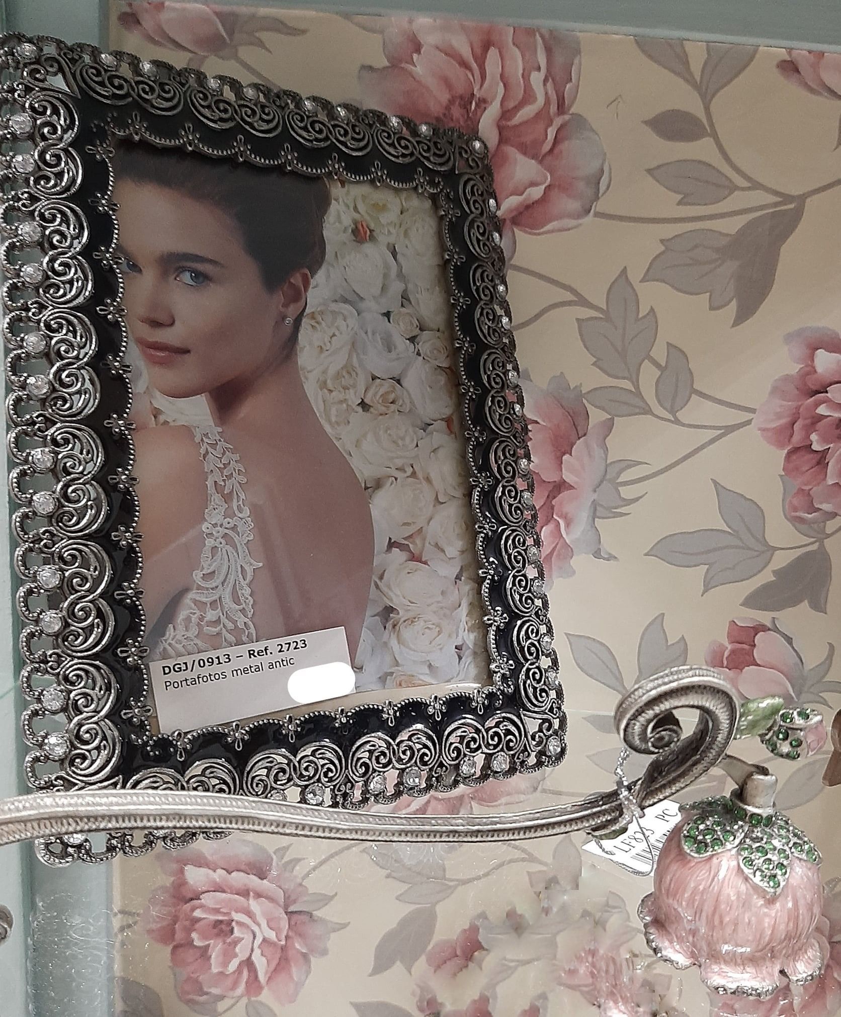 Marco de fotos adornado en plata con un retrato de mujer sobre un fondo de pantalla floral.