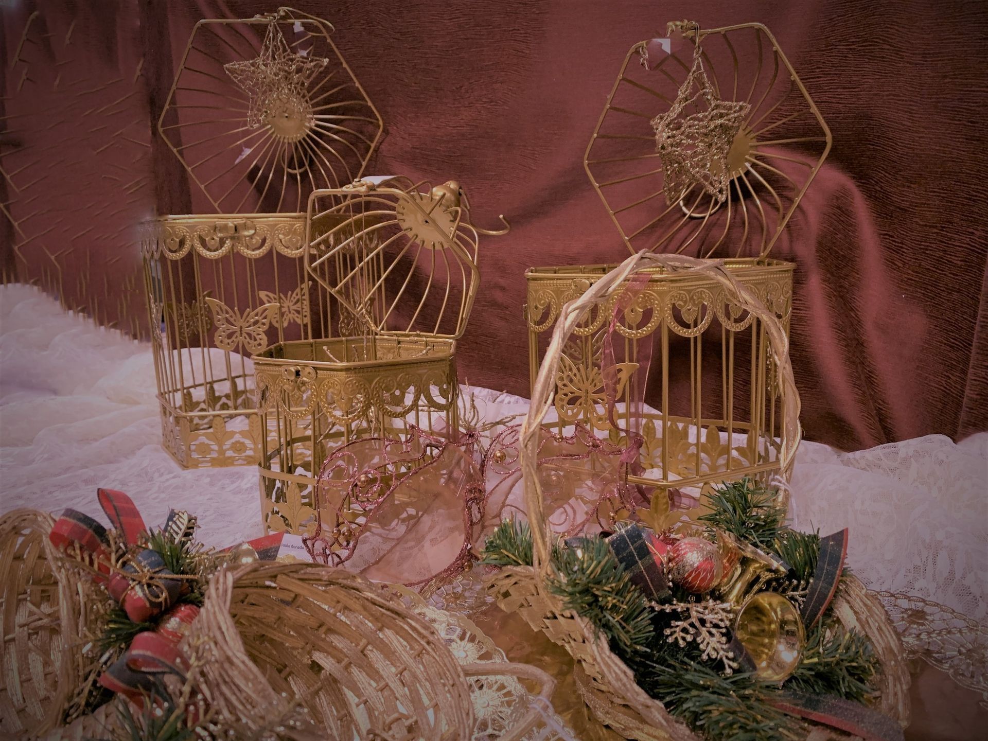 Jaulas de pájaros doradas sobre una superficie nevada con ramas decorativas sobre un fondo burdeos.