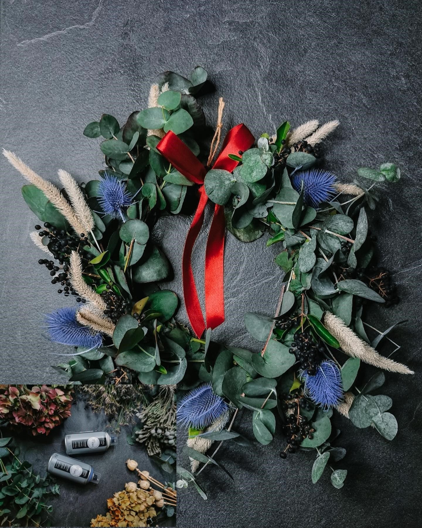 Corona con eucalipto, flores de cardo azul, un lazo rojo sobre fondo gris oscuro.