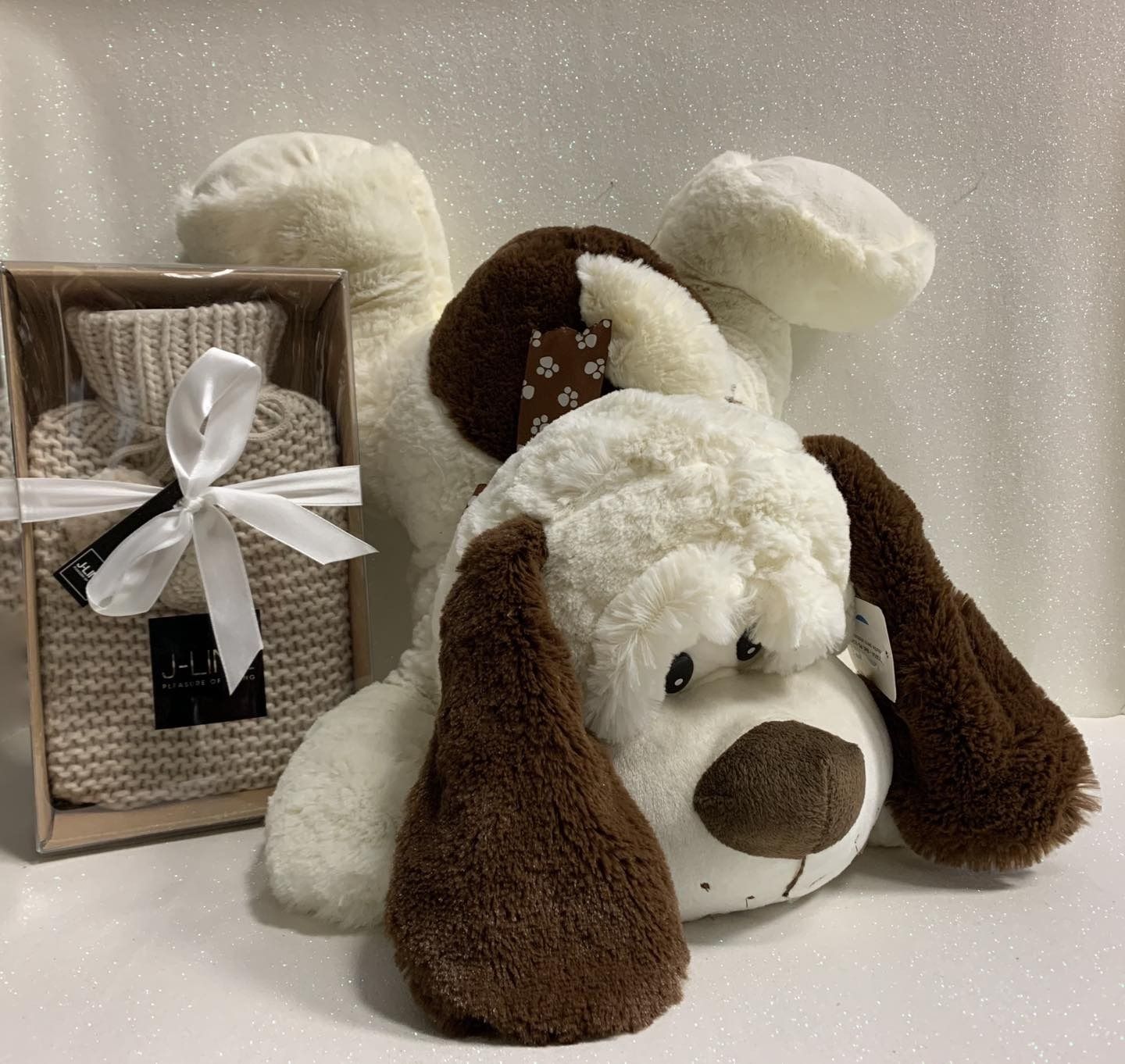 Juguete de peluche para perro con orejas marrones junto a una pequeña bolsa de agua caliente con funda de punto, atada con un lazo blanco.