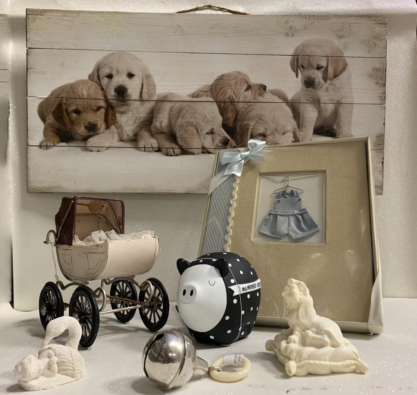Una colección de artículos para bebés: un cuadro con cachorritos, un cochecito, una alcancía, un marco de fotos y figuritas.