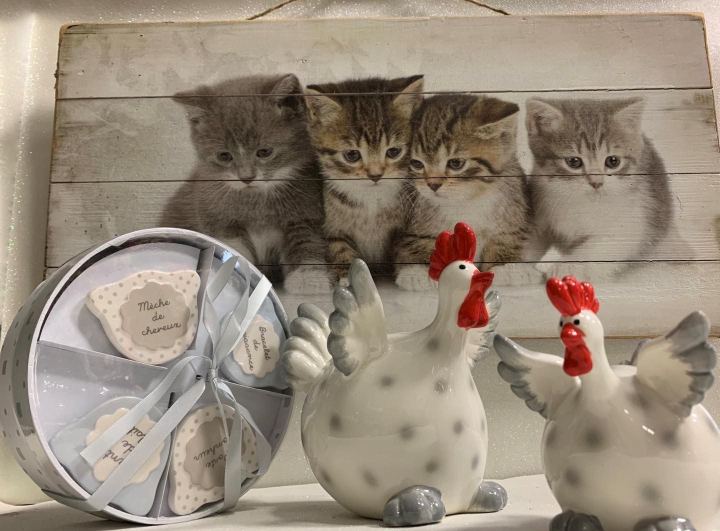 Una exhibición con ilustraciones de gatitos, dos pollos de cerámica y una caja de regalo con galletas atadas con una cinta.