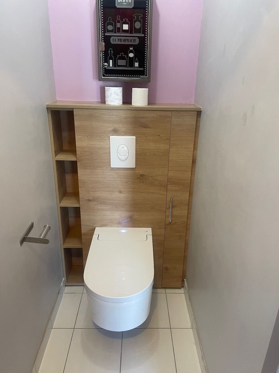 Dans une salle de bains étroite, des toilettes suspendues modernes sont équipées d'un meuble de rangement et d'une étagère imitation bois intégrés derrière.