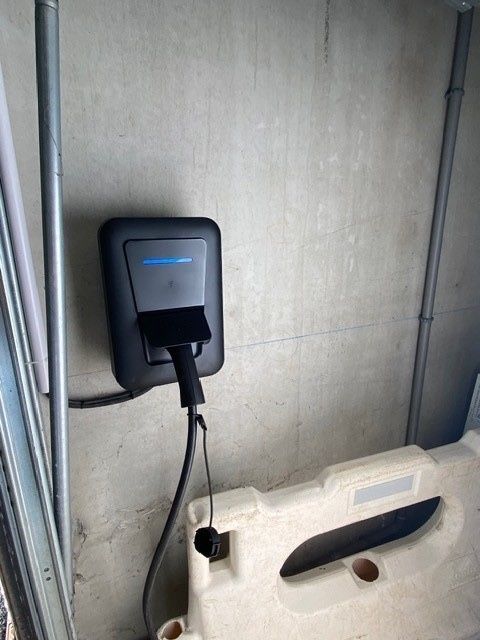 Une borne de recharge noire pour véhicules électriques, fixée sur un mur gris, avec un câble de recharge qui en pend.