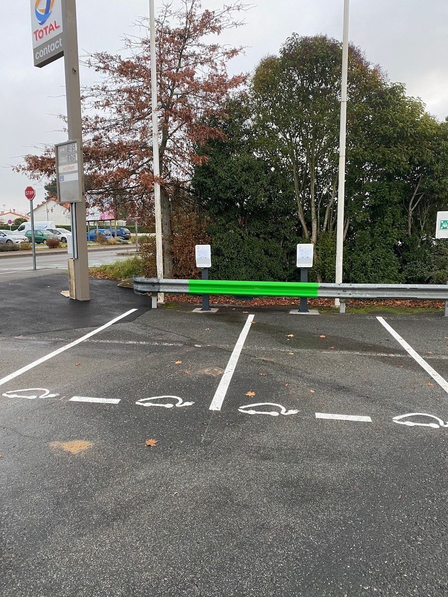 Deux places de stationnement réservées à la recharge des véhicules électriques dans une station-service, signalées par des symboles sur l'asphalte.