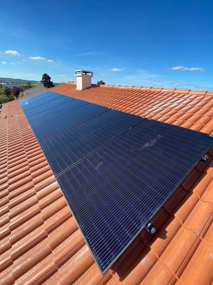 Une rangée de panneaux solaires sombres installés sur un toit de tuiles en terre cuite, sous un ciel bleu limpide.