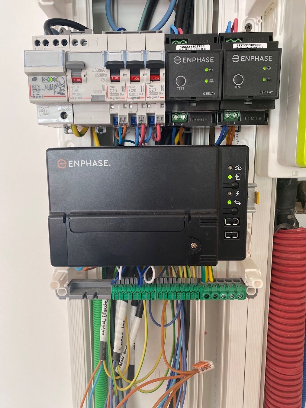 Une passerelle de surveillance solaire Enphase et des disjoncteurs électriques montés sur un panneau arrière blanc avec divers fils connectés.