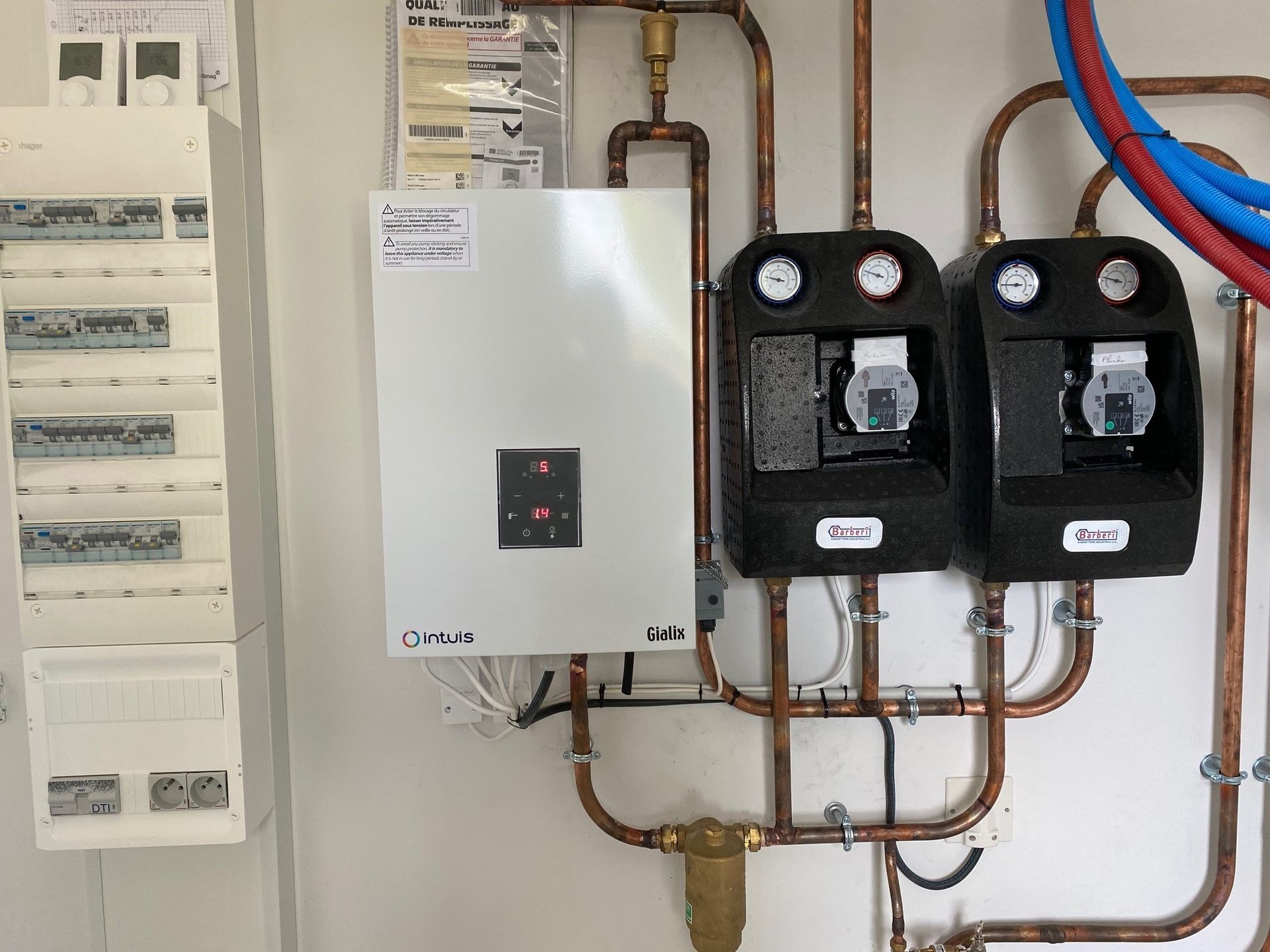Tableau électrique et système de chaudière avec tuyauterie en cuivre et deux stations de pompage montés sur un mur blanc.