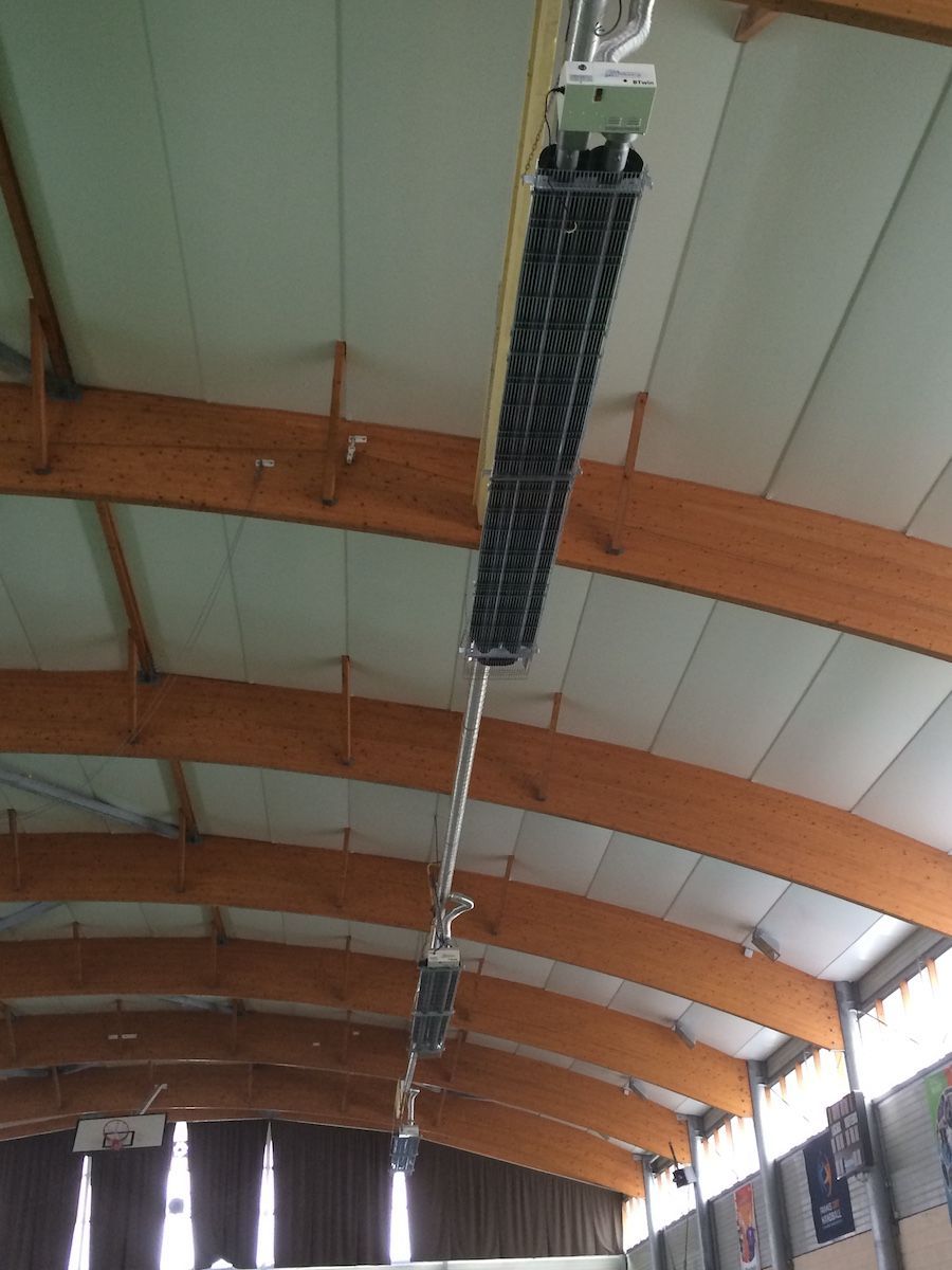 Vue en contre-plongée d'une série de radiateurs radiants industriels noirs fixés au plafond voûté en bois d'une grande salle.