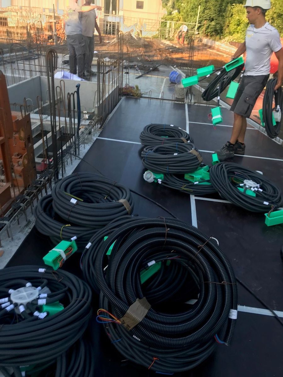 Des ouvriers du bâtiment préparent, sur une surface sombre, des bobines de conduit ondulé noir en vue de l'installation électrique.