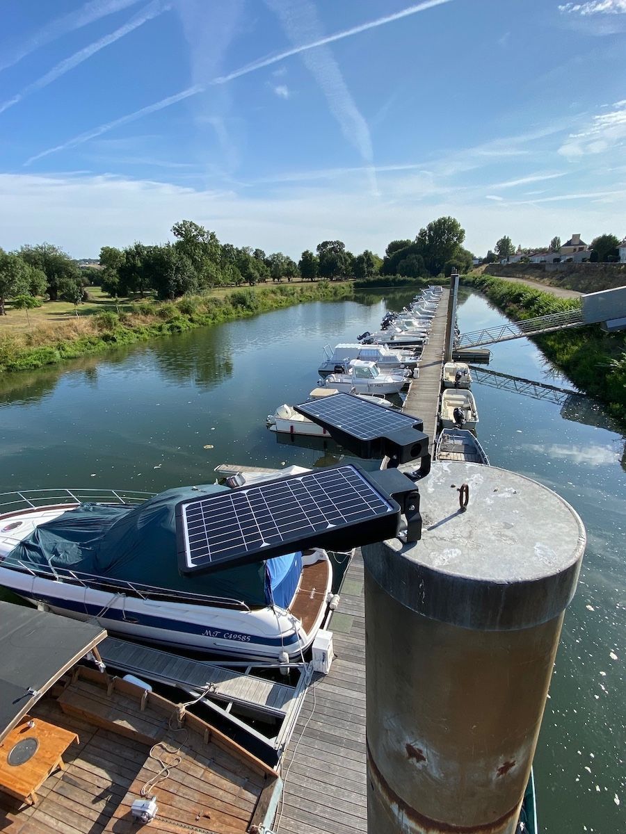 Des lampes solaires sont installées sur un pilier de quai surplombant une marina avec des bateaux amarrés sous un ciel bleu.