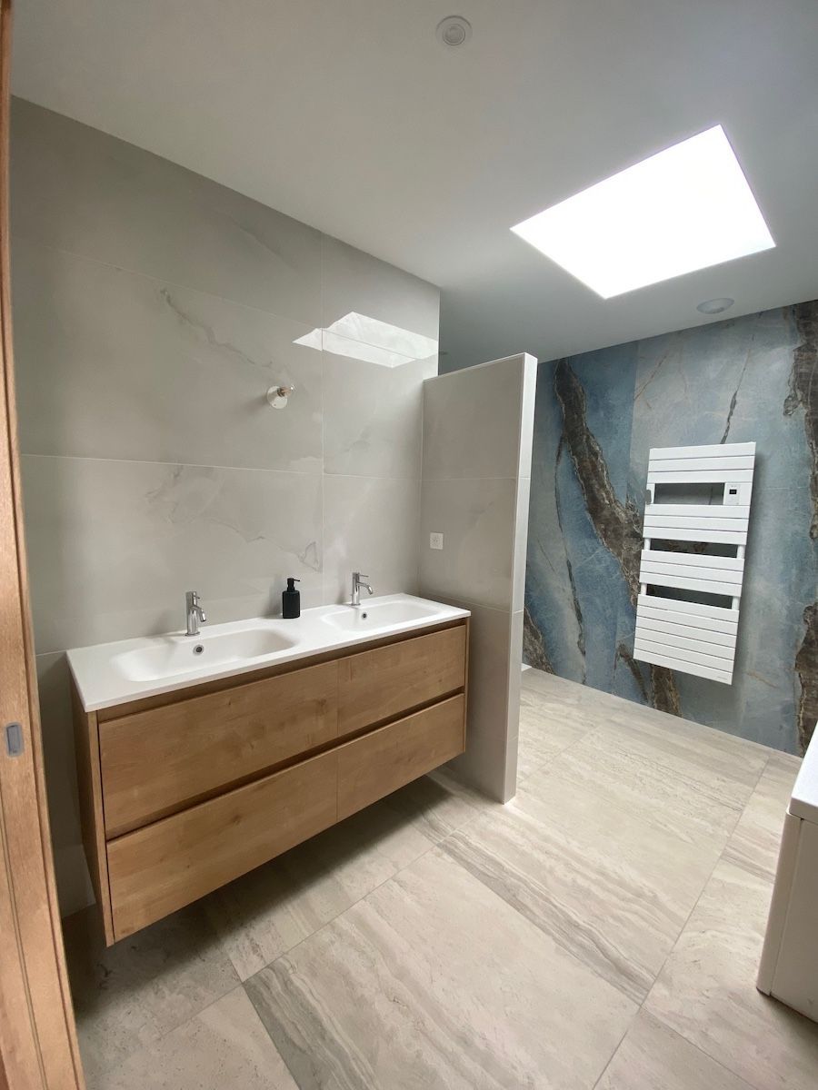 Une salle de bains moderne avec un meuble-lavabo double suspendu en bois, un sol en pierre claire, un muret et un mur d'accent bleu texturé.
