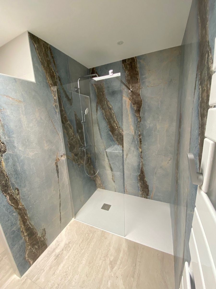 Une douche à l'italienne avec des panneaux muraux en marbre bleu et marron, une paroi en verre et un receveur de douche blanc.