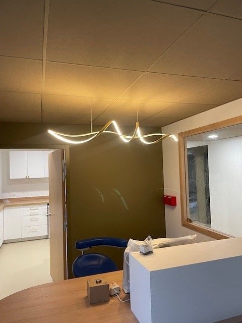 Dans un bureau aux murs couleur olive, une suspension lumineuse LED moderne et ondulée est suspendue au-dessus d'un comptoir d'accueil.