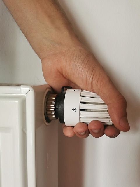 Une main ajuste le bouton d'un thermostat de radiateur blanc pour contrôler la température ambiante.