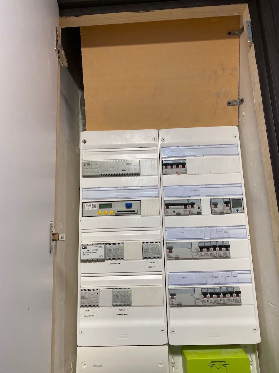 Un tableau électrique intérieur avec plusieurs disjoncteurs et un compteur numérique, le tout dans une armoire en bois.