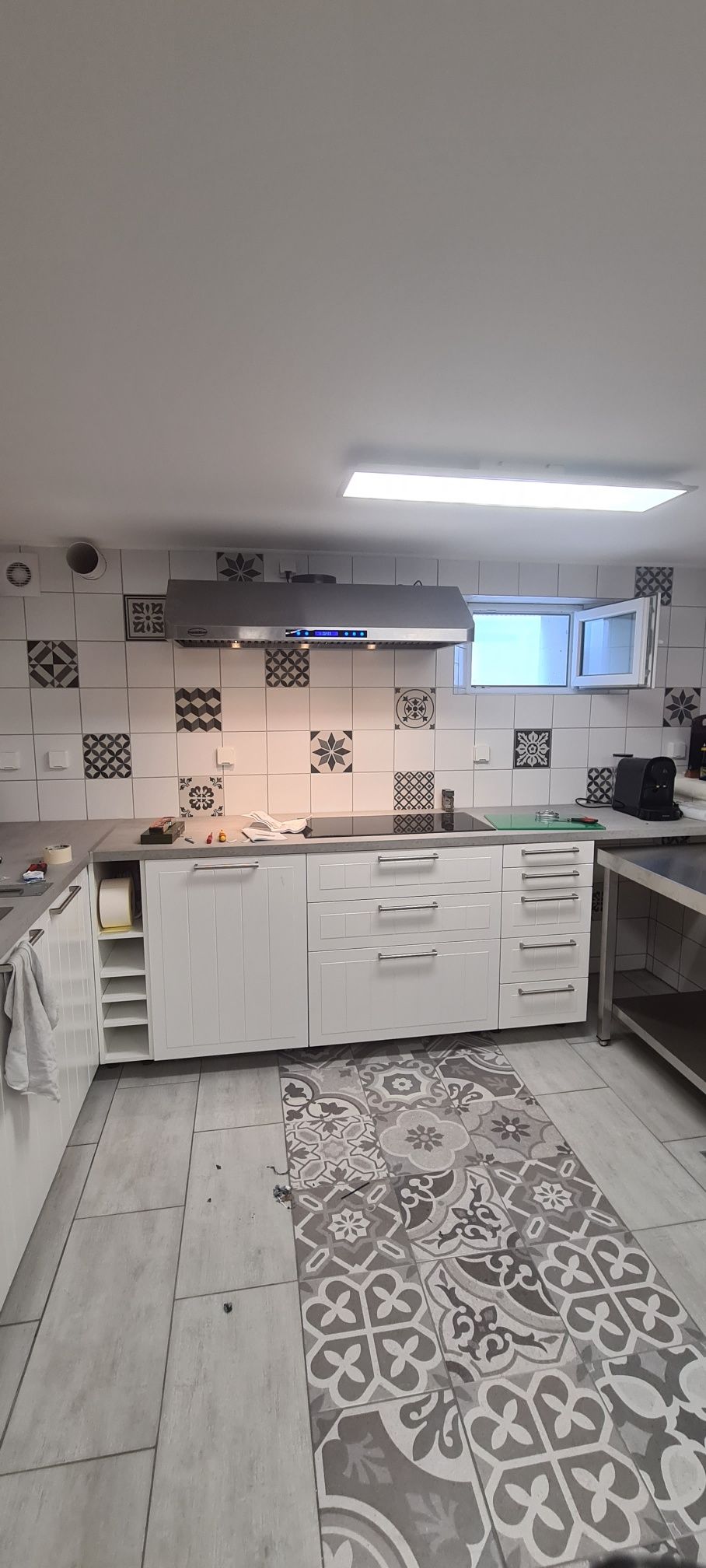 Une cuisine avec des armoires blanches, un dosseret à motifs, une hotte en acier inoxydable et un tapis à motifs sur le sol.