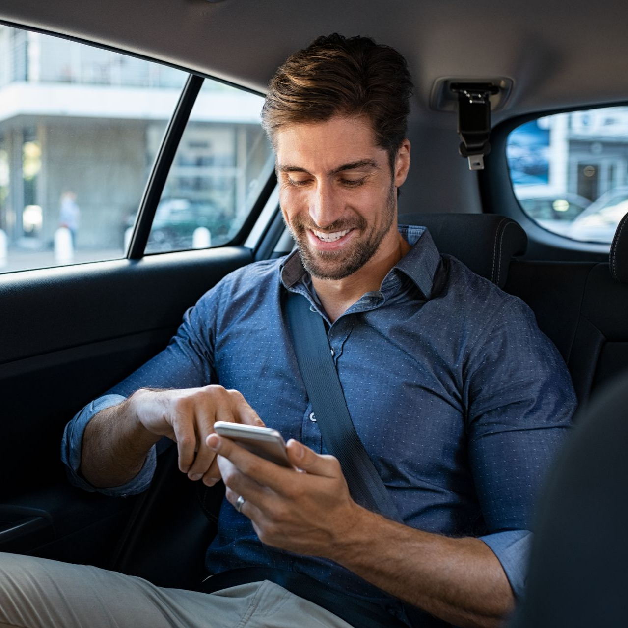 Homme souriant dans un taxi regardant son téléphone