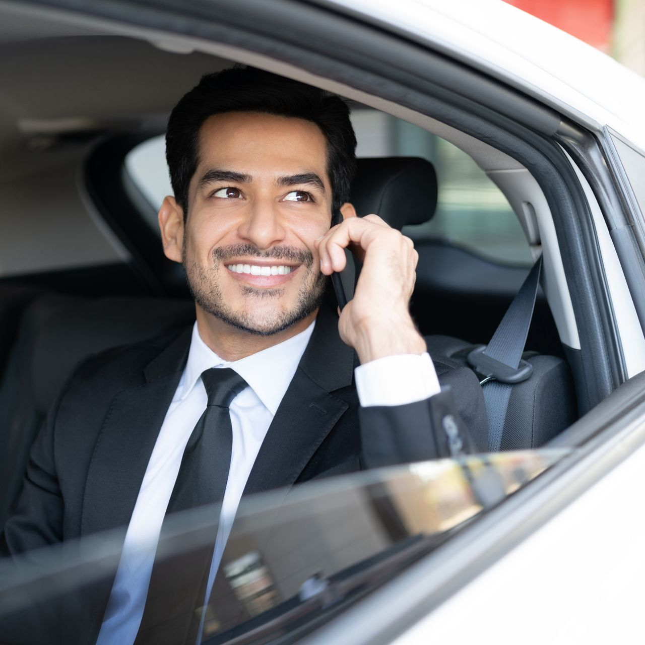 Homme souriant en costume au téléphone dans une voiture