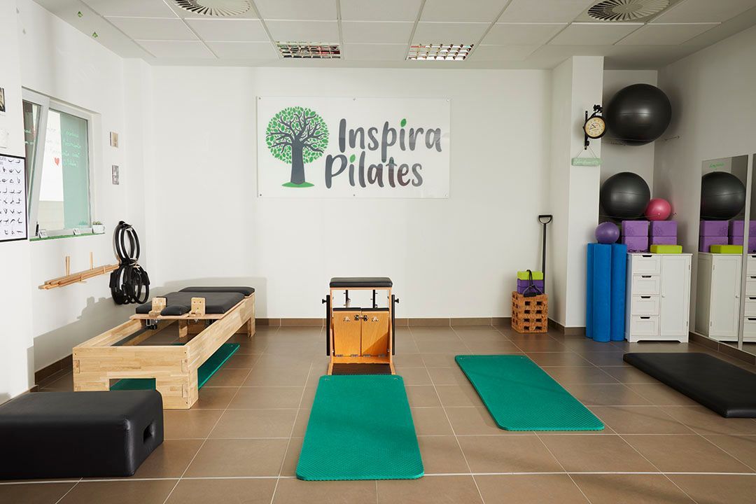 Estudio de pilates con equipamiento: reformer, silla, mats, pelotas y logo en la pared.