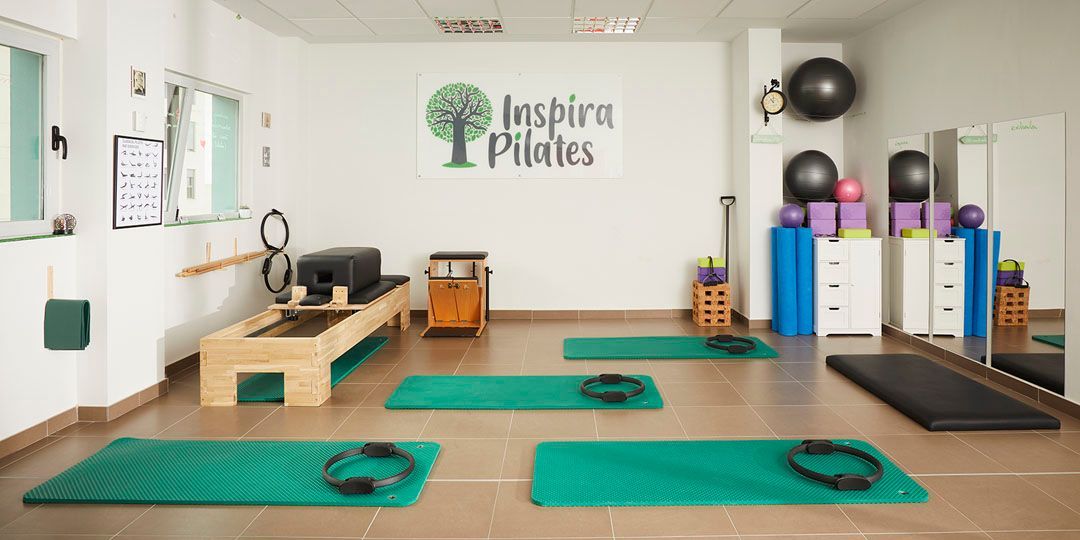Estudio de pilates con colchonetas verdes, equipamiento y un logotipo en la pared.