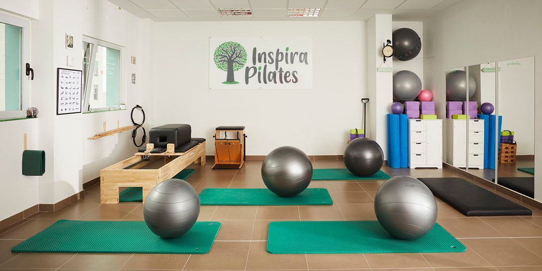 Estudio de pilates con pelotas de ejercicio, colchonetas y equipos; logotipo en la pared.