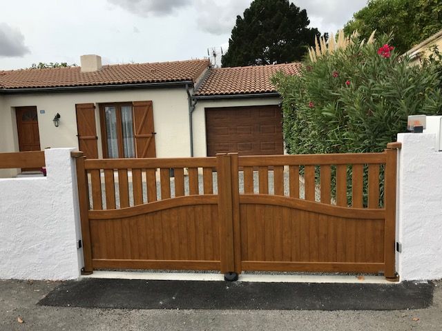 Portail en bois sur mur blancs devant une petite maison à la façade couleur crème 