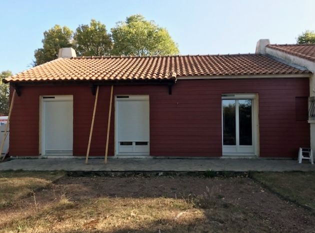 Bardage rouge foncé sur une petite maison aux fenêtres blanches et au toit en tuiles