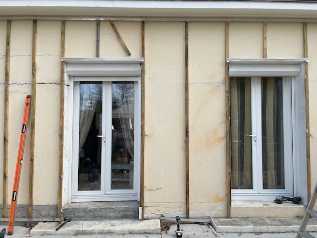 Mur extérieur avec deux portes-fenêtres blanches et des outils de construction appuyés contre elles