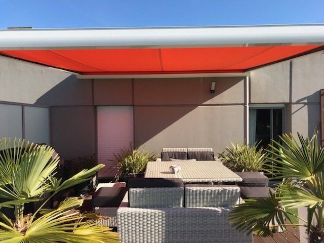 Pergola rouge sur façade noire couvrant une terrasse avec plantes et table