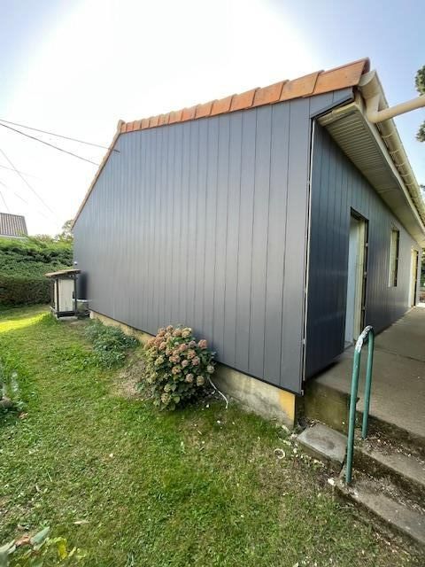 Maison à façade grise avec toit en pente, jardin gazonné et marches près de l'entrée.