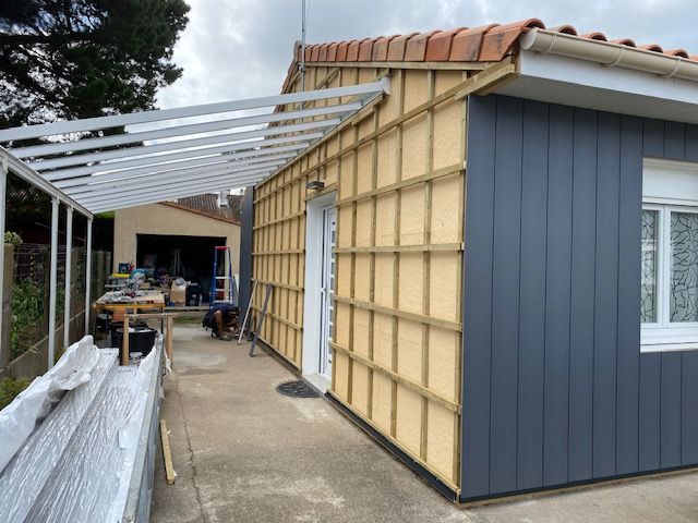 Bardage bleu foncé en cours de pose sur une maison avec pergolla blanche
