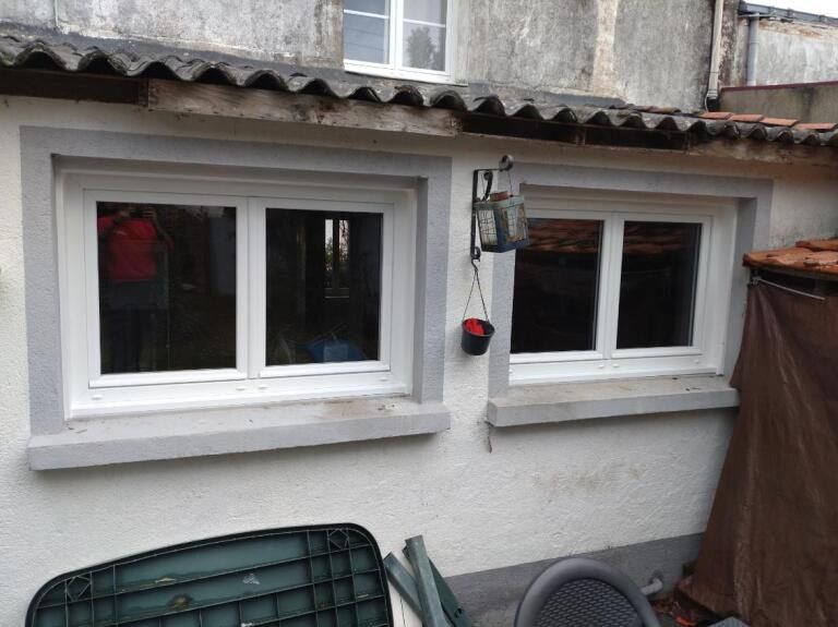 Deux fenêtres à cadre blanc sur un mur en stuc, avec une lanterne extérieure entre elles.