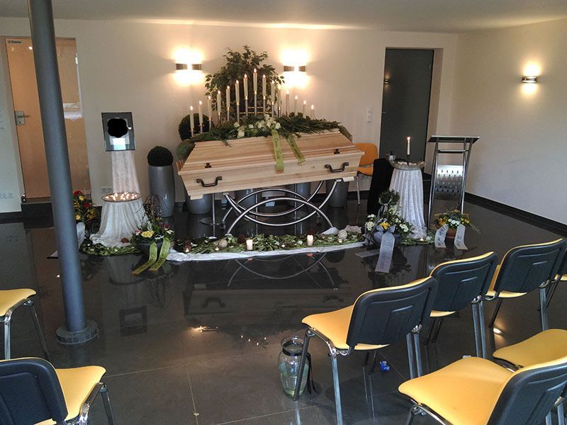 Holzsarg erhöhte Aufbahrung mit Blumenschmuck in einer Kapelle