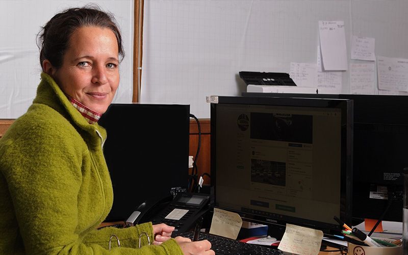 Eine Frau in einem grünen Pullover sitzt vor einem Computer.