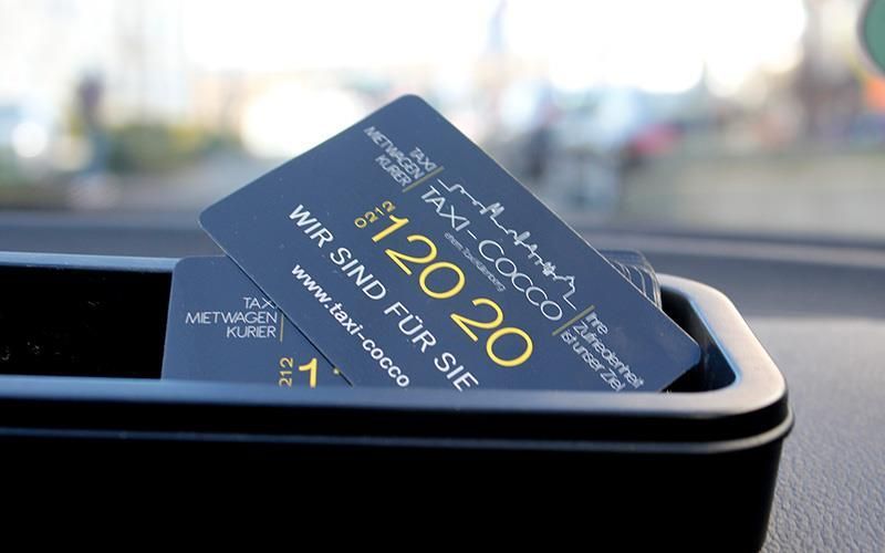 Zwei Visitenkarten liegen in einer Ablage auf dem Armaturenbrett eines Autos.