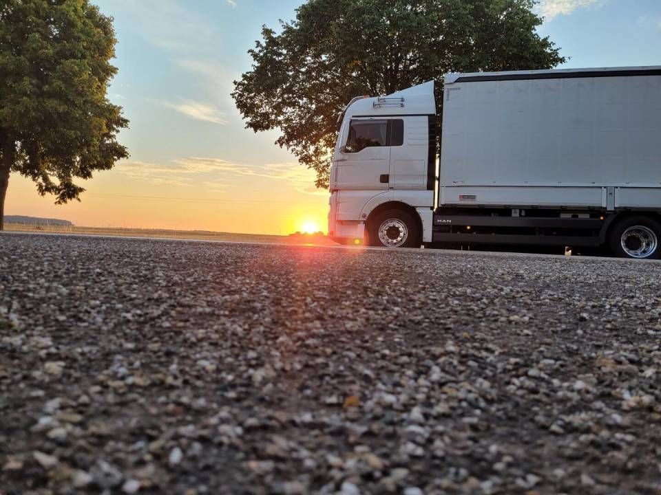 Ein Lastwagen parkt bei Sonnenaufgang am Strassenrand und zeichnet sich als Silhouette vor dem goldenen Himmel ab.