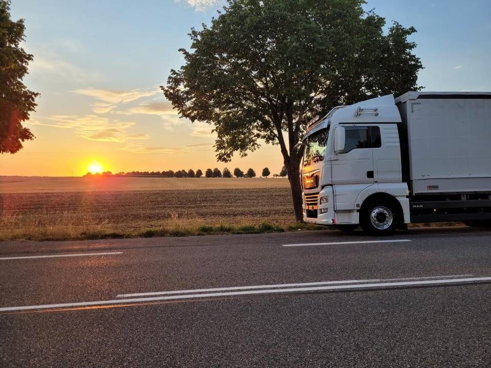 Ein weisser Sattelzug parkt bei Sonnenuntergang am Strassenrand, im Hintergrund ein Feld.