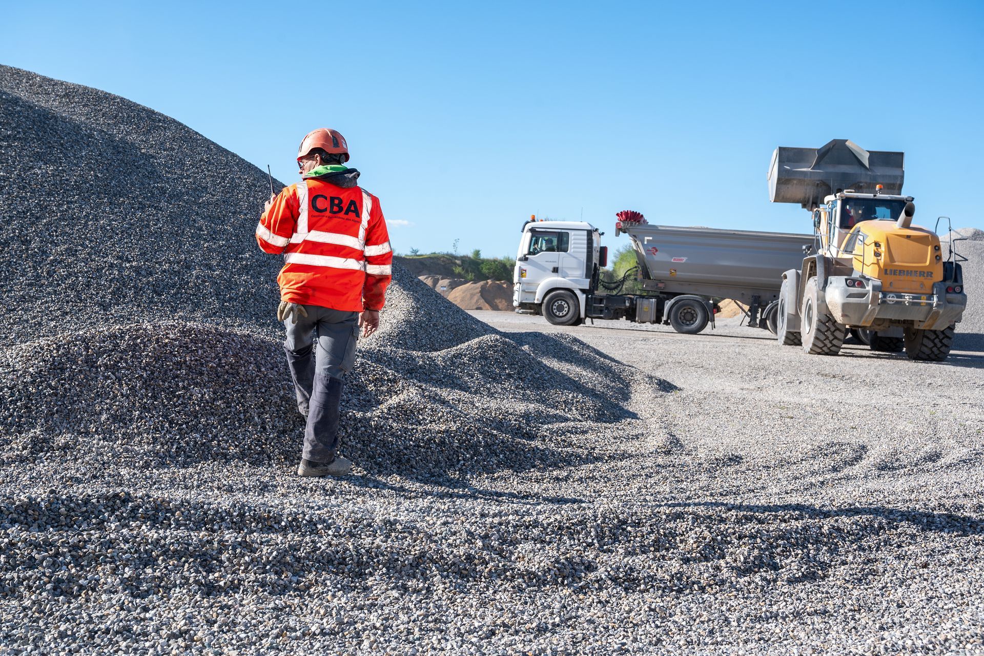 Membre de l'équipe CBA vu de dos, avec camion et chargeur en second plan