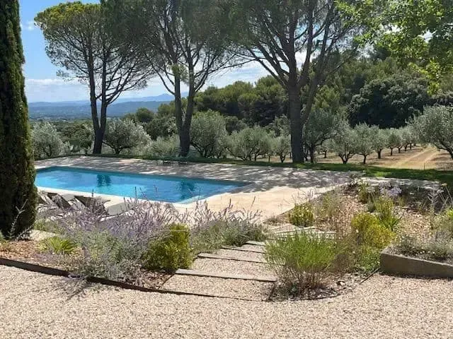 Piscine bordée d’une terrasse de jardin, avec des arbres et une vue sur les collines au loin